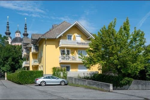 Kurzgasse 7 Willkommen in unserem modern und elegant gestalteten Wohnanlage, die von uns als Bauträger errichtet und verkauft wurden. Dieses Bild zeigt das schöne Äußere der modernen Gebäude, umgeben von Grün und Bäumen. Im Hintergrund können wir den klaren blauen Himmel und eine ferne Stadtlandschaft sehen. Diese Wohnanlage bietet luxuriöse Wohnräume, hochmoderne Annehmlichkeiten und eine friedliche Umgebung, die die Bewohner ihr Zuhause nennen können.